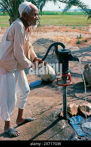 Älterer ägyptischer Mann pumpt Wasser aus der Erde mit einer Handpumpe im Freien Stockfoto