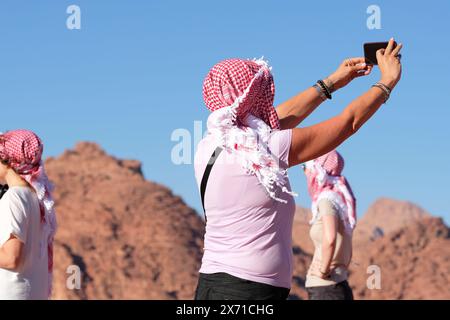 Wadi Rum, Jordanien Touristen halten an, um ein Foto-Selfie in der Wüstenlandschaft zu machen, die lokale Haschemitische Keffiyeh-Kopftücher tragen Stockfoto