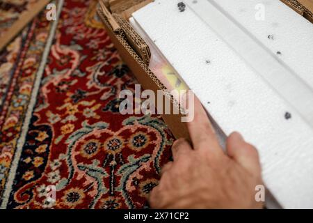 Eine Hand zeigt auf einen Artikel, der teilweise in einem Karton mit Polsterung aus Styropor liegt, was eine sorgfältige Inspektion und Interaktion mit der Verpackung anzeigt. Stockfoto