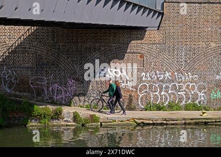 Blick vom Camley Street Natural Park of Regents Canal People mit dem Fahrrad unter Brücke durch Backsteinmauer Graffiti 2024 London England UK KATHY DEWITT Stockfoto