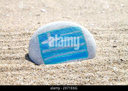 Griechische Landflagge auf dem Meeresstein auf leerem Sandstrand aus nächster Nähe gemalt. Urlaubskonzept. Stockfoto