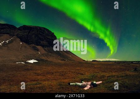 Eine Frau beobachtet, wie die Nordlichter allein auf einem Wiesen-Wiese in Island liegen. Romantische Frau in isländischer Frühlingsnächtelandschaft Island Reise Jagd Stockfoto