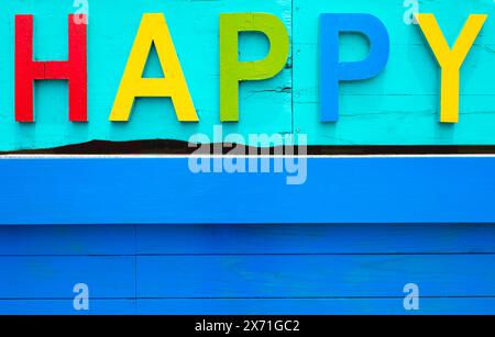 Bunte Buchstaben mit einem Wort glücklich, Text mit hölzernem Hintergrund. Bunte Buchstaben aus Holz auf grünem Hintergrund Stockfoto