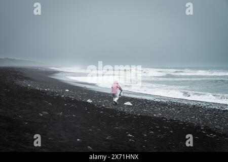 Touristenfrau mit blauem Eisberg am schwarzen Sandstrand von Diamond Beach, Island. Keine Diamanten am Diamantstrand im warmen Frühling. Klimaänderung ef Stockfoto