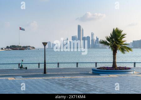 Abu Dhabi, VAE - 4. Januar 2024: Ein ruhiger Tag auf der Abu Dhabi Corniche mit der Skyline und einer lebhaften Flagge, die im Wind flattert. Stockfoto