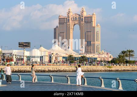 Abu Dhabi, VAE - 4. Januar 2024: Einheimische und Touristen genießen einen sonnigen Tag entlang der malerischen Uferpromenade von Abu Dhabi mit dem berühmten Bogen der Stadt Stockfoto