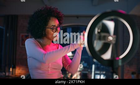 Schöne junge Frau richtet Studio Lighting und Smartphone ein, um eine Tanzroutine auf Video für soziale Medien aufzunehmen. Stilvolles schwarzes Mädchen in Brille streamt ihre Choreografie im Internet von zu Hause aus. Stockfoto