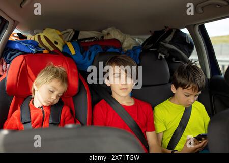 Drei Jungen auf Autositzen, unterwegs im Auto, schlafen und spielen auf dem Handy, während sie in den Urlaub gehen Stockfoto