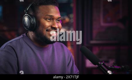 Gutaussehender junger afroamerikanischer Mann, der in das Mikrofon spricht, während er Radiosendung aus seinem Loft Apartment aufnimmt. Happy Black Male spricht vor der Kamera und nimmt Podcast Live in sozialen Medien auf. Stockfoto