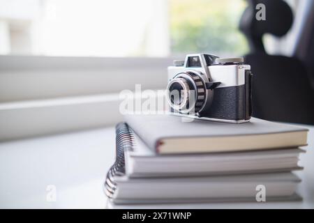 Eine Vintage-Filmkamera sitzt auf einem Tisch in einem Büro und ein Buch hebt sich im Hintergrund hervor. Eine Vintage-Filmkamera mit schlichtem Design sitzt auf einem Tisch Stockfoto