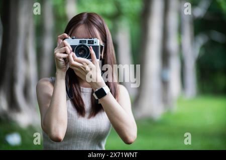 Die junge Fotografin hält eine Filmkamera im Vintage-Stil in der Hand und inspiziert die Filmkamera, um sie zu verwenden, nachdem Filmkameras bei der Fotografie populär geworden sind Stockfoto