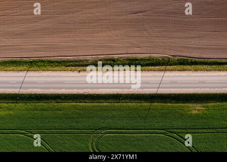 Vogelperspektive auf eine Straße, die durch ein riesiges Feld führt. Stockfoto