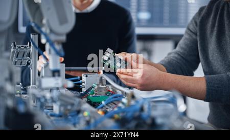 Männlicher Student tippt auf dem Tablet, während sein Klassenkamerad Microchip untersucht und Ideen teilt. Asiatischer Teenager, Der Microchip Hält. Moderne Technologien, Wissenschaft und Entwicklungskonzept. Nahaufnahme Stockfoto