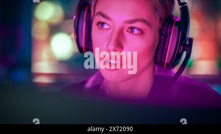 Nahaufnahme Porträt einer stilvollen jungen Frau mit kurzen Haaren, die am Abend zu Hause Online-Computervideospiel spielt. Gamer diskutieren Taktiken mit Teamkollegen, während er mit dem Headset spricht. Stockfoto