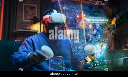 Filmisches Porträt eines jungen, stilvollen Schwarzen Mannes mit Virtual Reality-Headset. Afroamerikaner sitzt zu Hause auf einem Sofa und spielt VR-Spiel. Visualisierung des Gameplay-Konzepts. Stockfoto