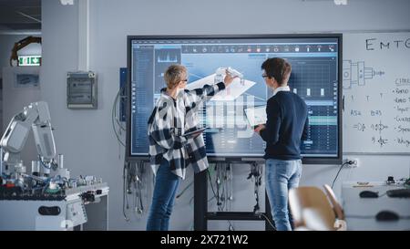 Die Schüler diskutieren die Arbeit von Robotic Hand, während sie sich den großen Bildschirm ansehen. Analyse von Diagrammen und Daten zum Schreiben eines Codes für Futuristic Device. Bildung und innovative Technologien. Stockfoto