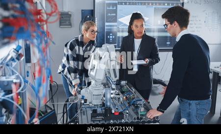 In Robotics Development Laboratory: Schwarze Lehrerin und zwei Schüler arbeiten mit Prototype of Robotic Hand. Junge Schülerin erzählt etwas mit einem Lächeln und arbeitet mit ihrem Team zusammen. Stockfoto