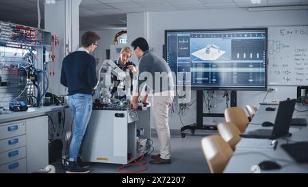 Ein vielfältiges Team von Studenten der Industrierobotik-Technik steht mit Roboterhand um den Tisch. Junge, der den Tablet-Computer hält, um den Roboter zu manipulieren und zu programmieren. Ausstattung Mit Digital Technology Konzept. Stockfoto