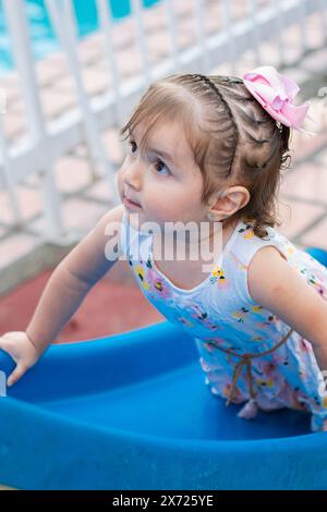 Das kleine Latina-Mädchen klettert auf der kleinen rutschigen Rutsche auf der anderen Seite Stockfoto