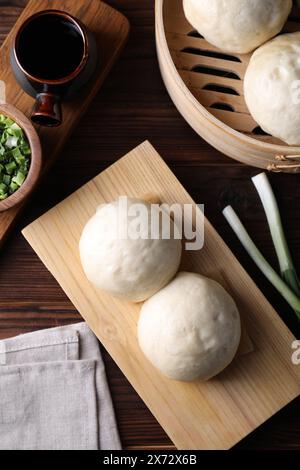 Köstliche chinesische gedämpfte Brötchen, grüne Zwiebeln und Sojasauce auf Holztisch, flache Ladefläche Stockfoto