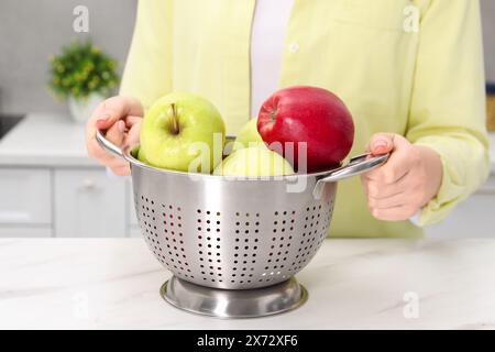 Frau, die ein Sieb mit frischen Äpfeln an einem weißen Marmortisch in der Küche hält, Nahaufnahme Stockfoto