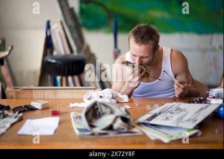 Junger Erwachsener Mann genießt einen Joint junger Erwachsener Mann genießt einen Joint mit Haschisch / Pot, während er auf einem Tisch in einem Kunststudio sitzt. Rotterdam, Niederlande. Rotterdam Kraakpand Merwehaven Zuid-Holland Nederland Copyright: XGuidoxKoppesxPhotox Stockfoto