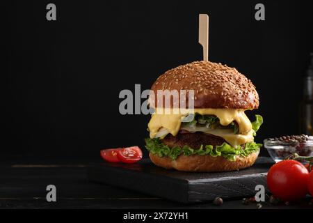 Leckerer vegetarischer Burger, Tomaten und Gewürze auf schwarzem Holztisch. Leerzeichen für Text Stockfoto