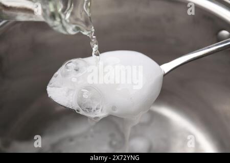 Essig in einen Löffel mit Backpulver über den Topf gießen, Nahaufnahme Stockfoto