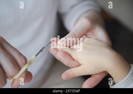 Nahaufnahme eines Erwachsenen, der die Fingernägel eines Kindes sorgfältig trimmt, um einen zarten Moment der Pflege und Pflege hervorzuheben. Stockfoto