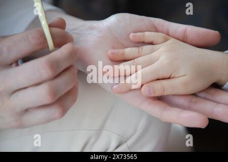 Nahaufnahme eines Erwachsenen, der die Fingernägel eines Kindes sorgfältig trimmt, um einen zarten Moment der Pflege und Pflege hervorzuheben. Stockfoto