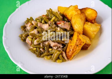 Grüne Bohnen mit Thunfischstück und gebackener Kartoffel auf weißem Teller auf grünem Hintergrund, Nahaufnahme. Stockfoto