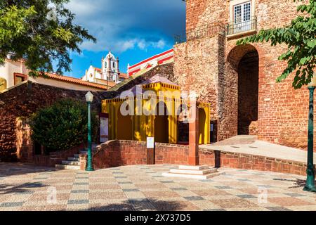 Blick auf Silves Stadtgebäude mit einem rot-weißen Torbogen und einem blauen Brunnen, Algarve Region, Portugal. Stockfoto