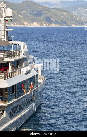 Besatzungsmitglied einer Luxusyacht, die in der Cannon Bay ankerte und die Außenfenster mit Seilen aus Portofino, Genua, Ligurien, Italien wäscht Stockfoto