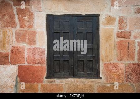 Detail der Fassade mit Steinmauer in warmen Tönen und einem geschlossenen schwarzen Holzfenster in der Mitte. Stockfoto