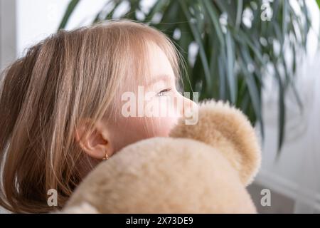 Kleines Kind, blondes Mädchen 4 Jahre alt spielt mit Spielzeug, umarmt Teddybären, glückliche Kindheit, erste Eindrücke, erzählt plüschigen Freund von Groll, beschwert sich Stockfoto