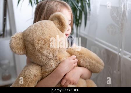 Kleines Kind, blondes Mädchen 4 Jahre alt spielt mit Spielzeug, umarmt Teddybären, glückliche Kindheit, erste Eindrücke, erzählt plüschigen Freund von Groll, beschwert sich Stockfoto