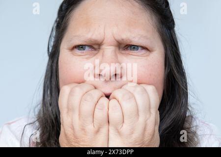 Die verzweifelte reife Frau mit langen Haaren, die nervös in die Nägel beißen, zeigt häusliche Gewalt Anzeichen von Angst und Trauma Stockfoto