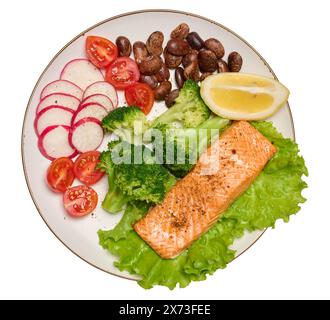 Gesundes Mittagessen mit gegrillter Forelle auf grünem Salat, neben Gemüse, Tomaten, Radieschen, Brokkoli und einer Portion Bohnen, isolierter Hintergrund Stockfoto