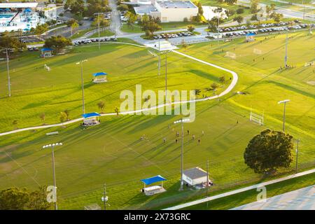 Blick aus der Vogelperspektive auf den öffentlichen Sportpark mit Kindern, die bei Sonnenuntergang im Grasstadion spielen. Aktives Lebenskonzept Stockfoto