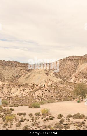 Wüstenlandschaft mit kleinen Tipi-Strukturen zwischen zerklüfteten Hügeln und karger Vegetation unter teilweise bewölktem Himmel Stockfoto