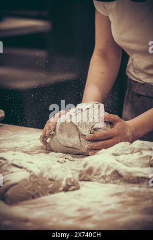 Eine Bäckerin kntet Brotteig in der Bäckerei. Vintage-Stil mit Körnung. Vertikal. Stockfoto
