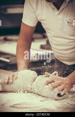 Ein Bäcker knetscht Brotteig in der Bäckerei. Vintage-Stil mit Körnung. Vertikal. Stockfoto