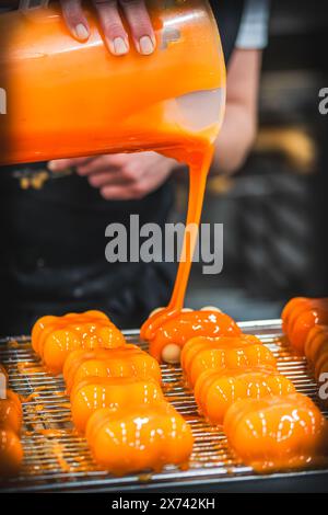 Konditorei, die Tartlets mit einer Orangenglasur bedeckt. Zubereitung der Tartlets durch einen professionellen Konditor. Stockfoto