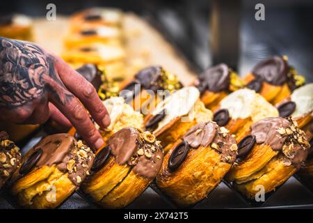 Die Hand des Konditors legt Tartlets mit Schokolade auf das Tablett. Zubereitung der Tartlets durch einen professionellen Konditor. Stockfoto
