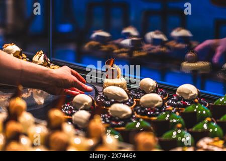 Die Hand einer Bäckerei-Verkäuferin legt glasierte Torten auf die Verkaufstheke. Vorbereitung am frühen Morgen für den Verkauf. Stockfoto