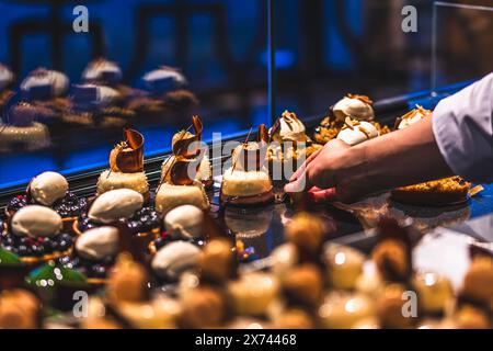 Die Hand einer Bäckerei-Verkäuferin legt glasierte Torten auf die Verkaufstheke. Vorbereitung am frühen Morgen für den Verkauf. Stockfoto