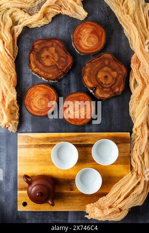 Teekanne und Tassen mit hölzernem Schneidebrett und Baumstammscheiben auf schwarzem Tafel Hintergrund. Flache Lagen. Draufsicht. Stockfoto