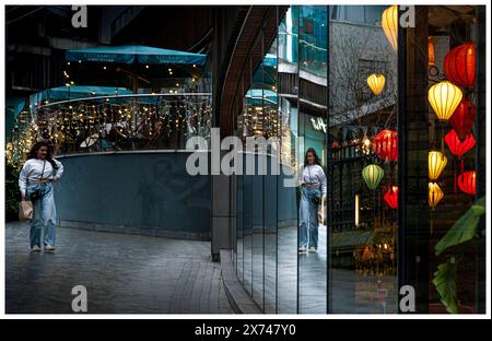 Einzelperson - nachts - Spaziergang durch das Einkaufszentrum, das sich in Restaurantfenstern spiegelt. Das Innere des Gebäudes hat aufgehängte, mehrfarbige chinesische Laternen Stockfoto