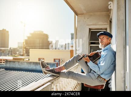 Künstler, Senior und Mann mit Akustikgitarre für das Spiel mit pensioniertem Musiker auf dem Balkon in der Stadt für Erinnerungen. Alt, kreativ und stolz auf Stockfoto