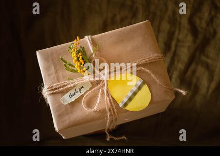 Geschenkschachteln mit einem Anhänger in Form eines Ostereies, verziert mit einer gelben Blume. Auf dunklem Hintergrund. Stockfoto